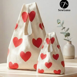 Two cream canvas tote bags featuring a red heart print standing on a light wooden table. The image displays the Aura Essential bag in two sizes, featuring a wide gusset and integrated handles, representing the finished result of this digital sewing pattern.