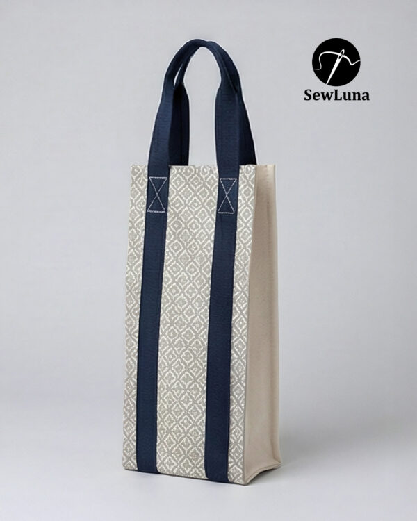 Handmade fabric wine carrier with blue straps and a grey geometric diamond pattern sitting next to a red wine bottle with a burgundy bow on a wooden table.