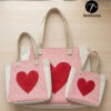 Three handmade cream and pink polka-dot canvas tote bags in small, medium, and large sizes featuring a large red heart applique on the front panel, displayed on a light wood surface.