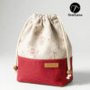 Finished example of the Bloom Essential Drawstring Pouch sewing pattern sitting on a wooden stool. The bag features a beige floral top section and a solid red canvas bottom with a leather handmade tag. It has a gathered drawstring top with cotton cord and wooden beads.