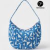 Model wearing the Azure Hobo Bag, a blue and white geometric print slouchy shoulder bag with a wide integrated strap. The bag has a curved crescent silhouette and is shown as a finished example of this digital sewing pattern.