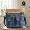 Blue patterned handmade canvas crossbody bag sitting on a wooden table near a window. This beginner-friendly PDF sewing pattern bag features a top zipper, adjustable navy strap, and two front pockets with a brown leather handmade tag.