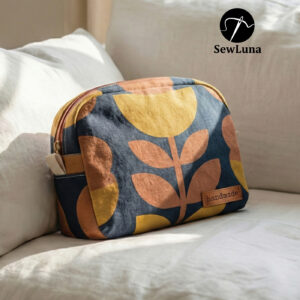 Two handmade curved zipper pouches in mustard yellow and navy blue botanical linen fabric sitting on a rustic wooden table. The larger toiletry bag stands behind a smaller matching cosmetic case which features a brown leather "handmade" label.