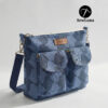 Blue patterned handmade canvas crossbody bag sitting on a wooden table near a window. This beginner-friendly PDF sewing pattern bag features a top zipper, adjustable navy strap, and two front pockets with a brown leather handmade tag.