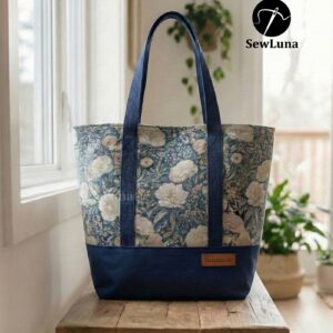 Finished Lyra canvas tote bag sewing pattern featuring a vintage blue floral tapestry upper, solid navy blue base, and navy webbing straps. The handmade bag is standing upright against a white background, showcasing this beginner DIY project.
