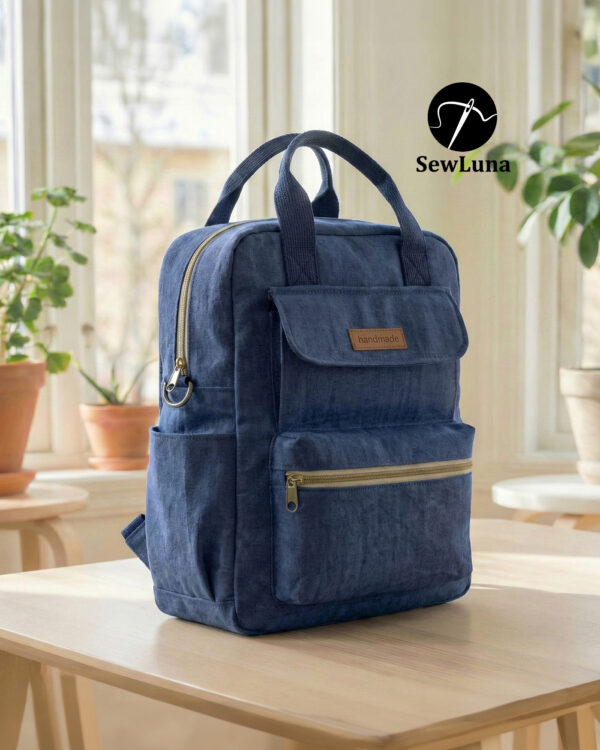 Finished blue canvas Piper Backpack with top handles, front flap, zipper pockets, and brass hardware against a clean white background. Sewing pattern example showcasing a structured, modern everyday bag.