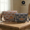 Two handmade curved crossbody bags in brown and navy geometric patterned fabric sitting on a wooden table. The DIY saddle bags feature flap closures with leather handmade tags and adjustable webbing straps.